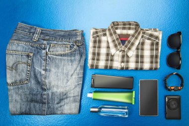 üstten görünüm güneş gözlüğü, kol saati, kamera, akıllı telefon ve hijyen seti mavi arka plan üzerinde seyahat için rahat kıyafet. Yukarıdan görüntülemek