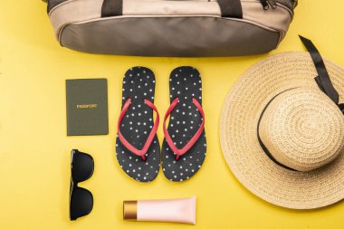 üstten görünüm Bagaj çanta, şapka, terlik, losyon, güneş gözlüğü ve sarı arka plan üzerinde seyahat pasaport. Yukarıdan görüntülemek