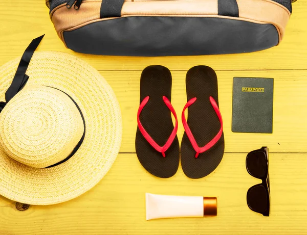 female stuff such as luggage bag, hat, slippers, lotion, sunglasses and passport for traveling on wooden table background. View from above