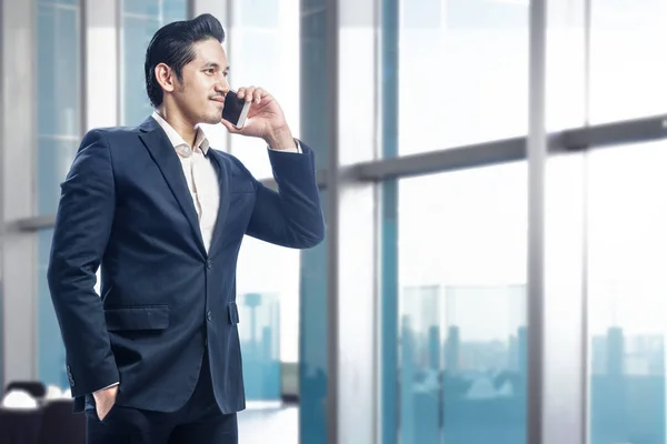 Handsome asian businessman standing while talking on the cellphone in office