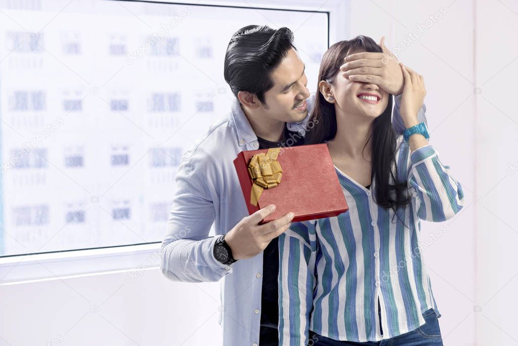 Cheerful asian man covering her girlfriend eyes and giving a gift. Love concept and Valentines day