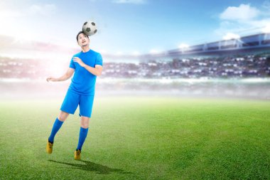 Genç Asyalı futbol oyuncu başlık topu Stadyumu arka plan üzerinde