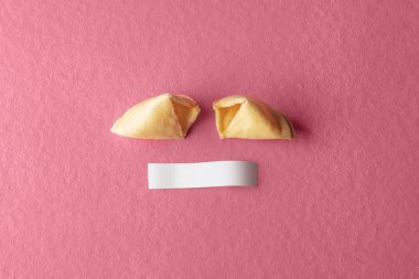 Cracked fortune cookie with blank paper on pink background