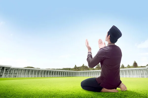 亚洲男子坐在草地上祈祷的位置上的后视 举起手来 凝望着清真寺外的天空 — 图库照片