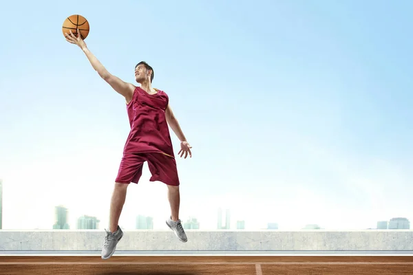 高いジャンプ男前な男性バスケット ボール選手とリバウンド ボール風景と青い空を背景に屋外のバスケット ボール コートで得点するには — ストック写真