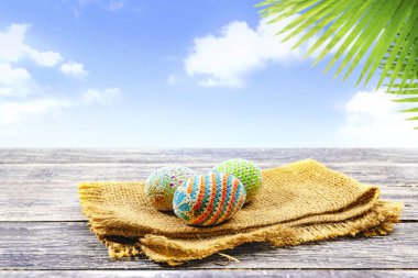 Palmiye yaprakları ve mavi gökyüzü arka plan ile ahşap masa kumaş üzerinde renkli Paskalya yumurtaları. Mutlu Paskalya