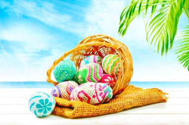 Renkli Paskalya yumurtaları kumaş ve ahşap masa palm Şubeler ve mavi gökyüzü arka plan ile mavi okyanus ile ahşap sepet döktüm. Mutlu Paskalya