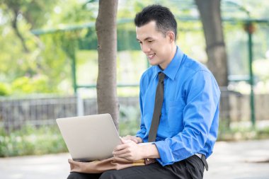 Oturma ve laptop ile parkta üzerinde çalışma Asya işadamı gülümseyen