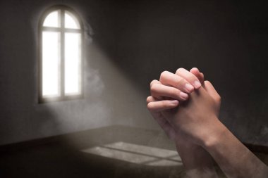 Erkek eller dua pozisyonunda odanın içinde, pencerelerden gelen ışıkla.