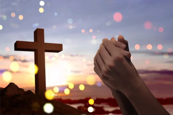 Christian cross and male hands with praying position over sunset background