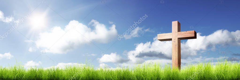 Christian cross on the green grass with sunlight over blue sky background