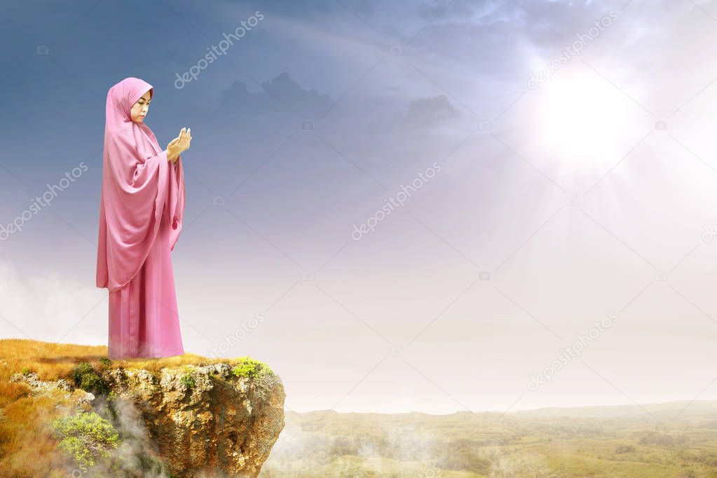 Asian muslim woman in veil raised hands and praying on the edge 