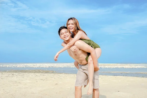 Счастливый азиат с девушкой на спине на пляже — стоковое фото