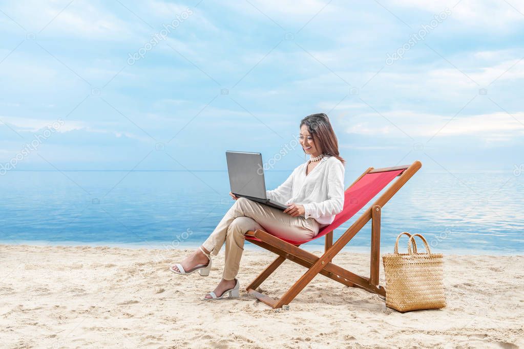 Asian business woman working with laptop sitting in the beach ch