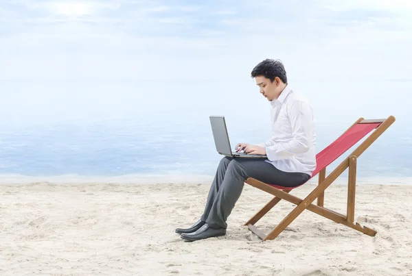 Empresário asiático trabalhando com laptop sentado na cadeira de praia — Fotografia de Stock
