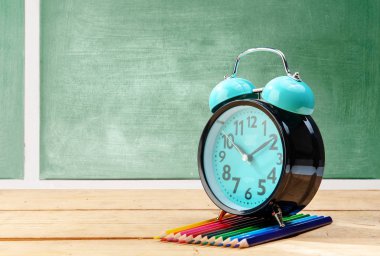 Tahta tahtalı tahta üzerinde çalar saat ve renkli kalemler 