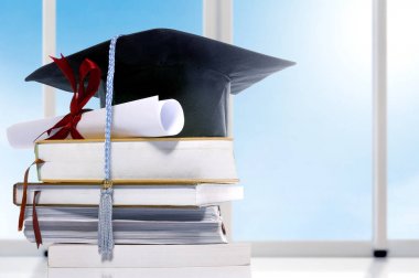 Mezuniyet şapkası ve masada kitap yığını üzerinde diploma