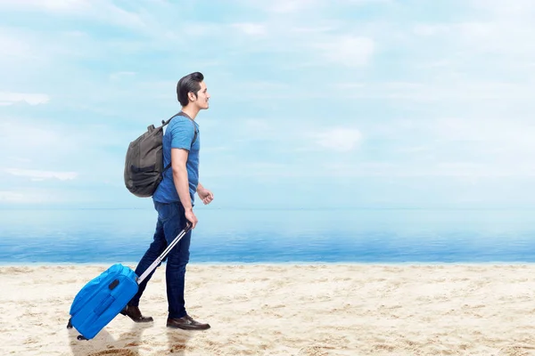Bavul çantası ve sırt çantası ile Asyalı adam sahilde yürüyüş — Stok fotoğraf