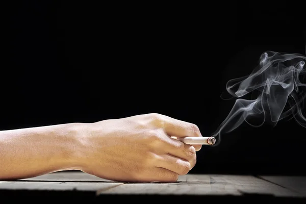 Hand vasthouden van een sigaret op houten tafel — Stockfoto