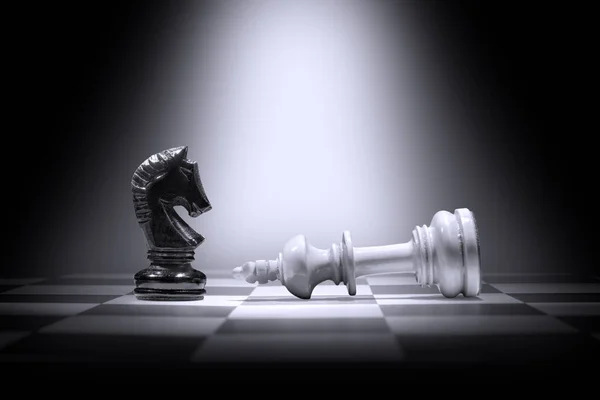 White king chess piece defeating by black knight chess piece