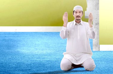 Asyalı Müslüman adam ellerini kaldırdı ve dua pozisyonda oturan