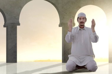 Asyalı Müslüman adam ellerini kaldırdı ve dua pozisyonda oturan
