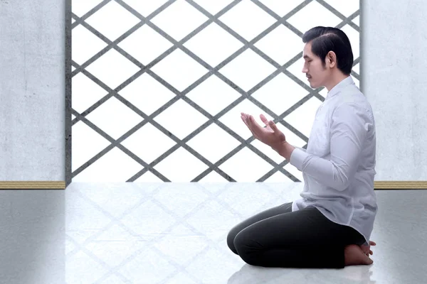 Мусульманин-азиат сидит, подняв руки и молясь — стоковое фото