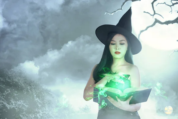 Asiatique sorcière femme dans chapeau apprend le sort à partir du livre magique — Photo