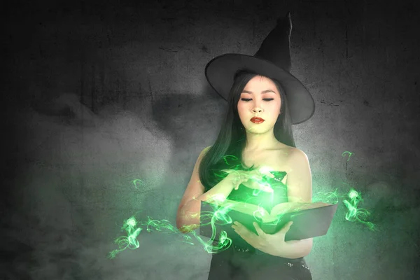 Ázsiai boszorkány nő kalapban megtanulja a varázslatot a bűvös könyv — Stock Fotó