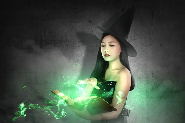 Mujer bruja asiática con sombrero aprende el hechizo del libro de magia —  Fotos de Stock