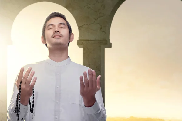 Asian Muslim man standing and praying with prayer beads while ra — Stock Photo, Image