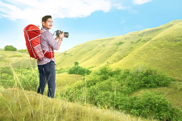 Asian man with a backpack holding a camera to take pictures — Stock Photo, Image