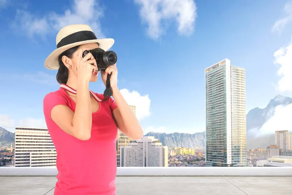 Asian woman in hat takes a picture of the modern city with her c — Stock Photo, Image