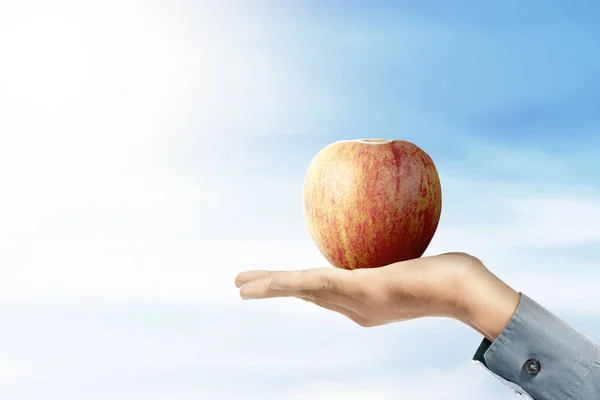 Humano sosteniendo la fruta de manzana con un fondo de cielo azul —  Fotos de Stock