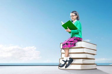 Kitap ve yeniden yığını üzerinde oturan gözlük ile Asya sevimli kız