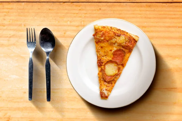 Slice of pizza on the plate with spoon and fork on wooden table — Stock Photo, Image