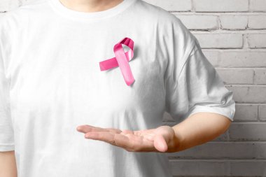 Beyaz tişörtlü bir kadın pembe farkındalık kurdelesi takıyor.