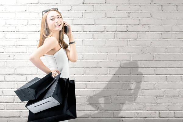 Mujer asiática usando el teléfono móvil mientras sostiene negro compras —  Fotos de Stock