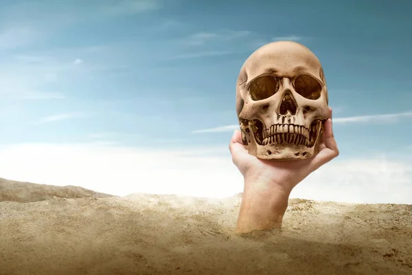 Hand raised from sand while holding a human skull — ストック写真