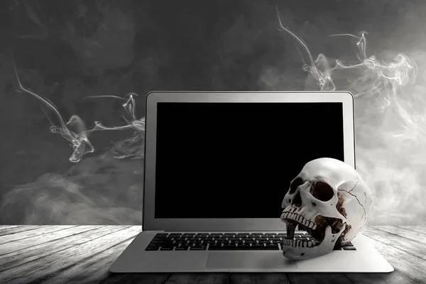 Laptop and human skull on a wooden table