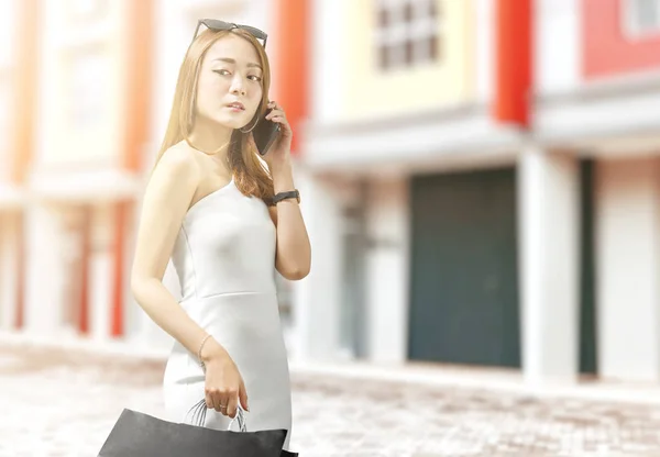 Ázsiai nő használja a mobiltelefont, miközben a kezében fekete vásárlás — Stock Fotó