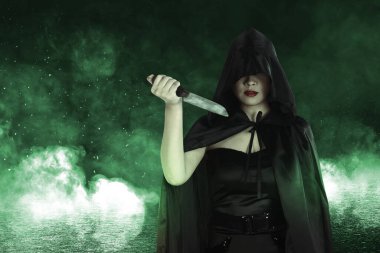 Siyah pelerinli Asyalı cadı elinde bir bıçakla mistik bir ateş tutuyordu.