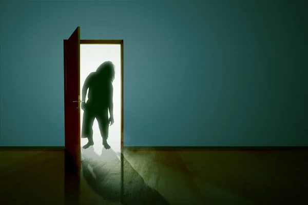 Silhouette of zombie standing on the opened door in the dark room