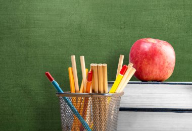 Kağıt bir sepetin içinde karatahta arka planda elma ve kalemle dolu bir yığın kitap. Okul konseptine dönüş