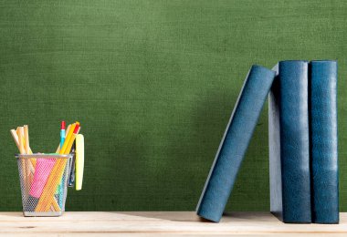 Kağıt bir sepetin içinde bir sıra kitap ve kalemle yazı tahtası arkaplanlı bir masa. Okul konseptine dönüş