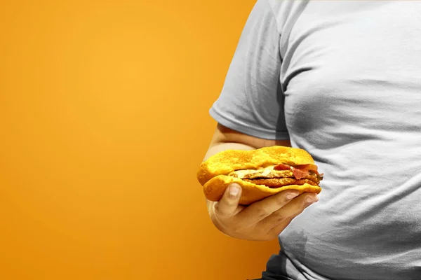 拿着一个有彩色背景的汉堡包的胖子 垃圾食品概念 — 图库照片