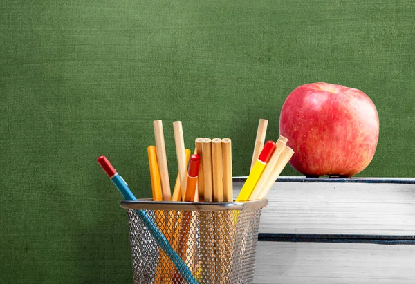 Stack of books with apple and pencil in a stationery basket with a chalkboard background. Back to School concept