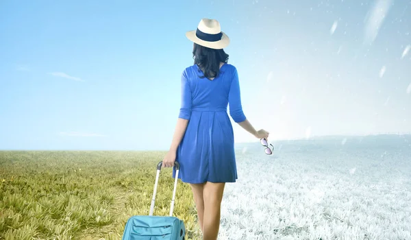 Asian woman with suitcase standing on the meadow field with winter and summer climate. Concept of changing the environment
