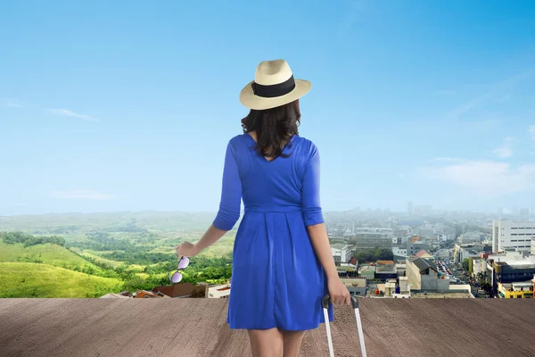 緑色の風景と青い空を背景にした都市を見てスーツケースを持つアジアの女性 環境を変えるという概念 — ストック写真