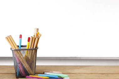 Sabit bir sepetin içinde kalem ve beyaz tahta arka planda boya kalemi. Okul konseptine dönüş